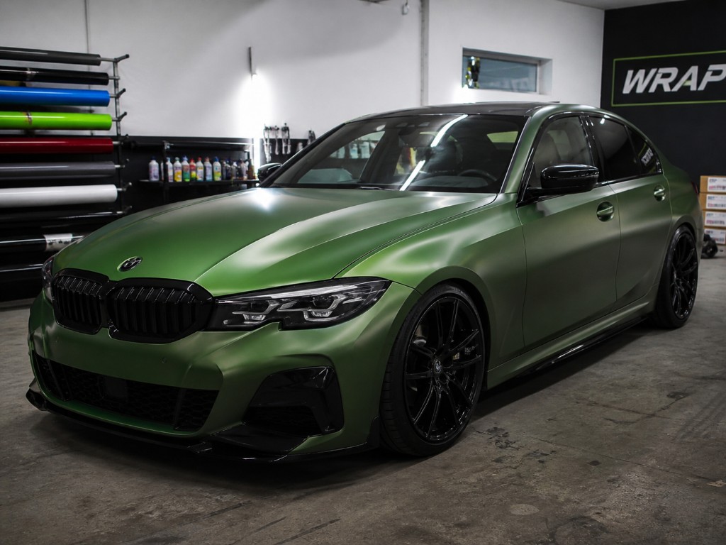 Vollfolierung: BMW Limousine in matt-metallic Olivgrün in der Werkstatt, Folienrollen und WRAP-Ambiente im Hintergrund